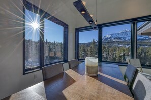 Une chambre moderne dotée de grandes fenêtres offrant une vue sur les montagnes, d’une table en bois et d’une lampe.