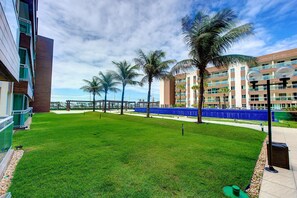Un espacio verde bien cuidado con palmeras y un edificio moderno de varios pisos y balcones.