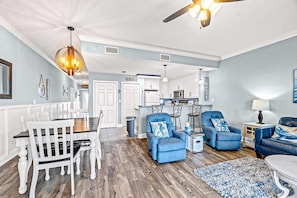 A spacious living room with a dining area, a kitchen in the background, and a ceiling fan. - Fourth Floor Condo with Shared Pool, Ocean View, High-Speed WiFi, & Washer/Dryer (Mexico Beach)