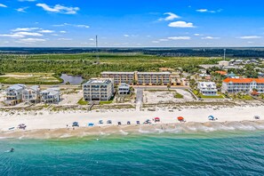 A coastal hotel with multiple buildings, a beach with umbrellas, and a view of the ocean. - Fourth Floor Condo with Shared Pool, Ocean View, High-Speed WiFi, & Washer/Dryer (Mexico Beach)