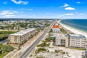 A coastal cityscape with a beachfront hotel featuring multiple floors, a swimming pool, and a road running parallel to the beach. - Fourth Floor Condo with Shared Pool, Ocean View, High-Speed WiFi, & Washer/Dryer (Mexico Beach)