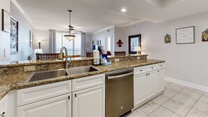 Una cocina moderna con encimeras de granito, muebles blancos, un lavamanos de acero inoxidable y lavavajillas integrado.