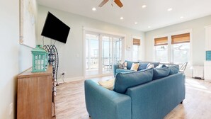 A living room with a blue sofa, a wooden cabinet, a ceiling fan, and a TV mounted on the wall. - Dog-friendly oceanfront home with a hot tub, washer&dryer & central AC (Cape San Blas)