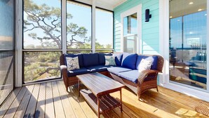 A covered outdoor seating area with a wicker sofa and a wooden table, large windows, and a view of the outdoors. - Dog-friendly oceanfront home with a hot tub, washer&dryer & central AC (Cape San Blas)
