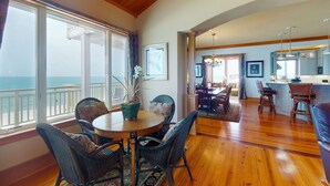 A spacious living area with a wooden floor, a dining table with chairs, a view of the ocean through large windows, and a kitchen area with bar stools. - Gorgeous beachfront home - washer/dryer, deck & central AC - community pool (St. George Island)