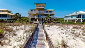 A beachfront property with a wooden boardwalk leading to a multi-story house with balconies. - Gorgeous beachfront home - washer/dryer, deck & central AC - community pool (St. George Island)