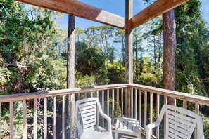 A wooden deck with two white chairs, surrounded by trees and a clear sky. - Snowbird friendly home near the beach with deck, outdoor shower, laundry (St. George Island)