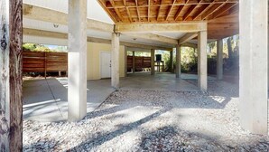 Ein offener, überdachter Außenbereich mit Betonsäulen und Holzbalkendecke, umgeben von Kies und einem Zaun.