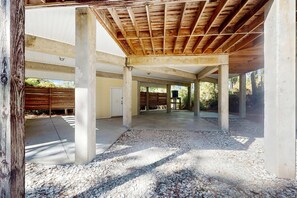 An open, covered outdoor area with concrete pillars and a wooden ceiling, surrounded by gravel and a fence. - Snowbird friendly home near the beach with deck, outdoor shower, laundry (St. George Island)