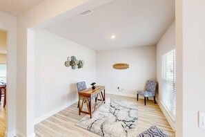 A spacious room with a wooden floor, a marble-patterned rug, a wooden side table, two patterned chairs, and a wall clock.