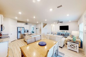 A spacious living area with a wooden dining table, a sofa, and a TV mounted on the wall.