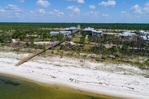 An aerial view of a coastal resort with multiple buildings, a beach, and a wooden bridge.