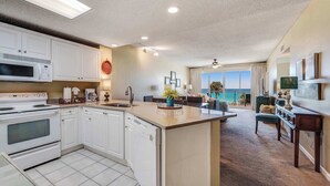 A modern kitchen with white cabinets, a large island, and a view of the ocean through the living area. - Stunning, waterfront home with Gulf views, pool & fitness room access (Destin)