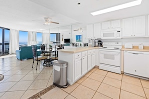 A modern kitchen with white cabinets, a central island, and a dining area with a view. - Beautiful Condo, Multiple on-site pools w hot tub & splash pad (Destin)