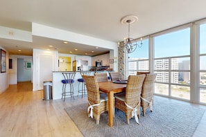 A modern kitchen with white cabinets, a microwave, and a dining area with wicker chairs and a wooden table. - Inviting & bright condo w shared on-site amenities - walk to the beach (Destin)
