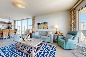 A modern living room with a sofa, armchair, coffee table, and dining area. - Inviting & bright condo w shared on-site amenities - walk to the beach (Destin)