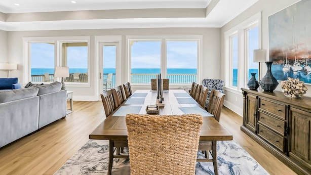 A spacious dining area with a view of the ocean, a large sofa, and a modern dining table. - Scenic waterfront home with five bedrooms & easy beach access - dog-friendly (St. George Island)