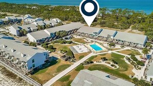 Vista aérea de un complejo turístico con varias edificaciones, una piscina y acceso a la playa.