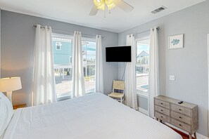 Ein Schlafzimmer mit Bett, Kommode, Stuhl, Fernseher und einem Fenster mit Vorhängen.