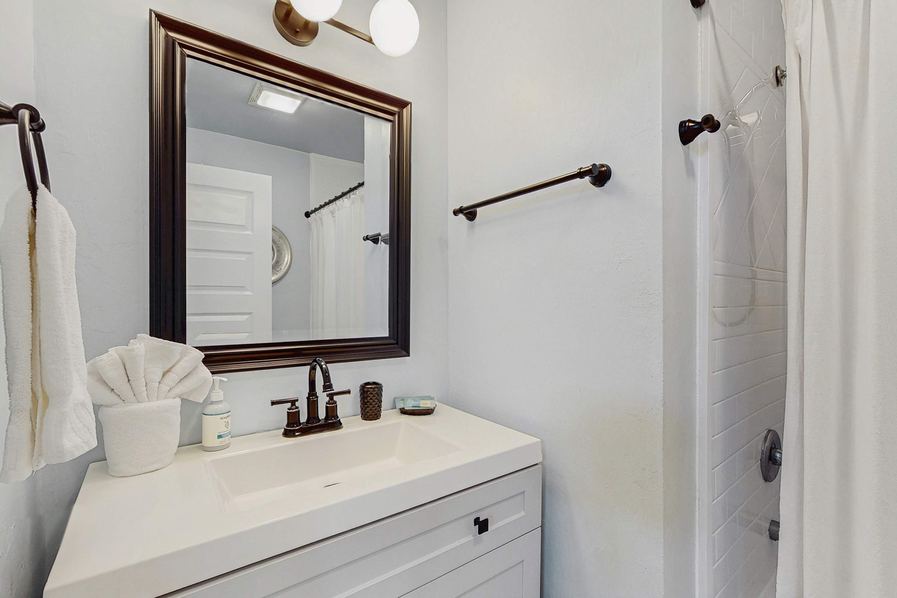 A bathroom with a white sink, a mirror with a wooden frame, a towel rack, and a shower curtain.
