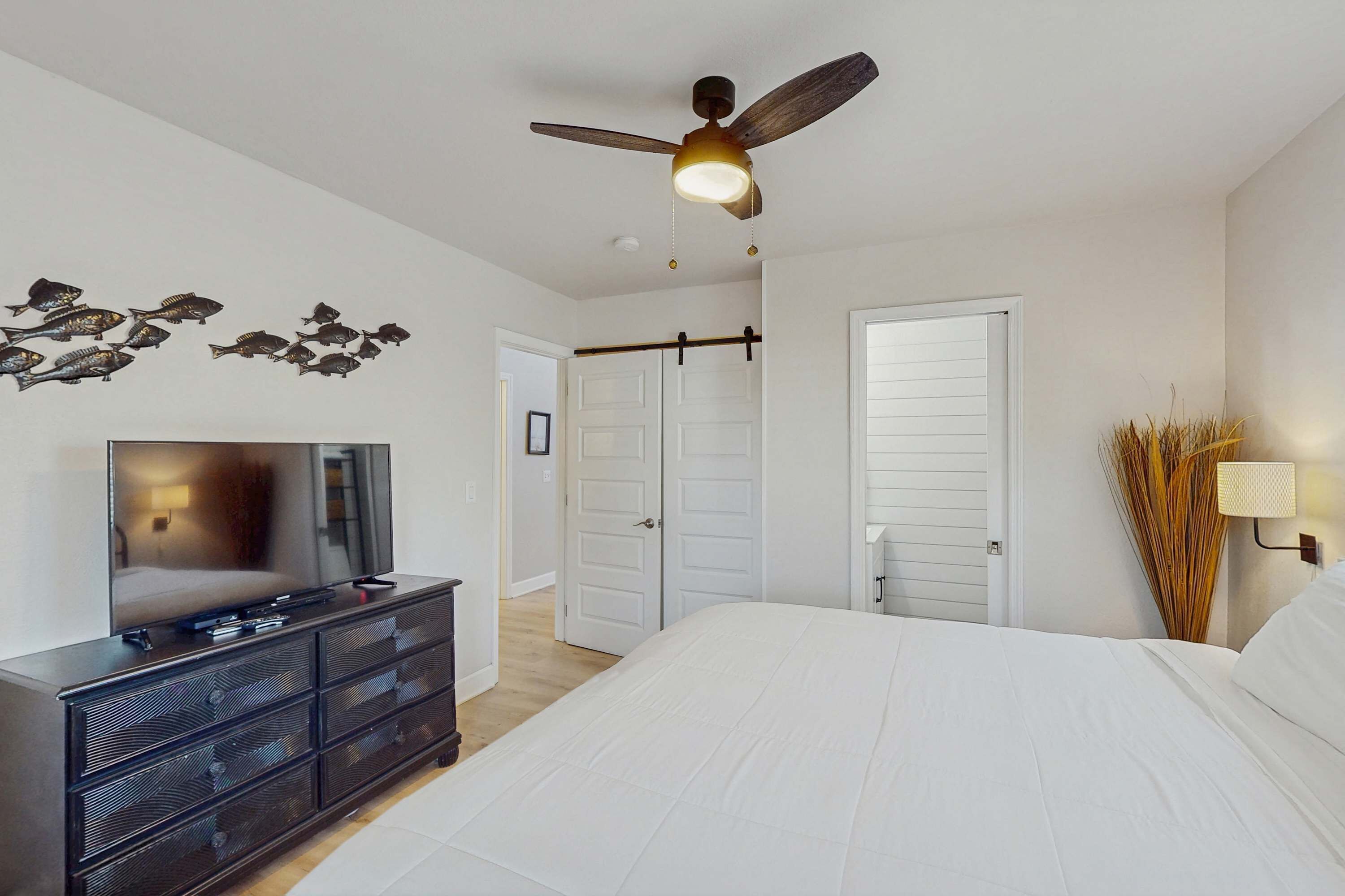 A bedroom with a bed, a dresser, a ceiling fan, and a TV.