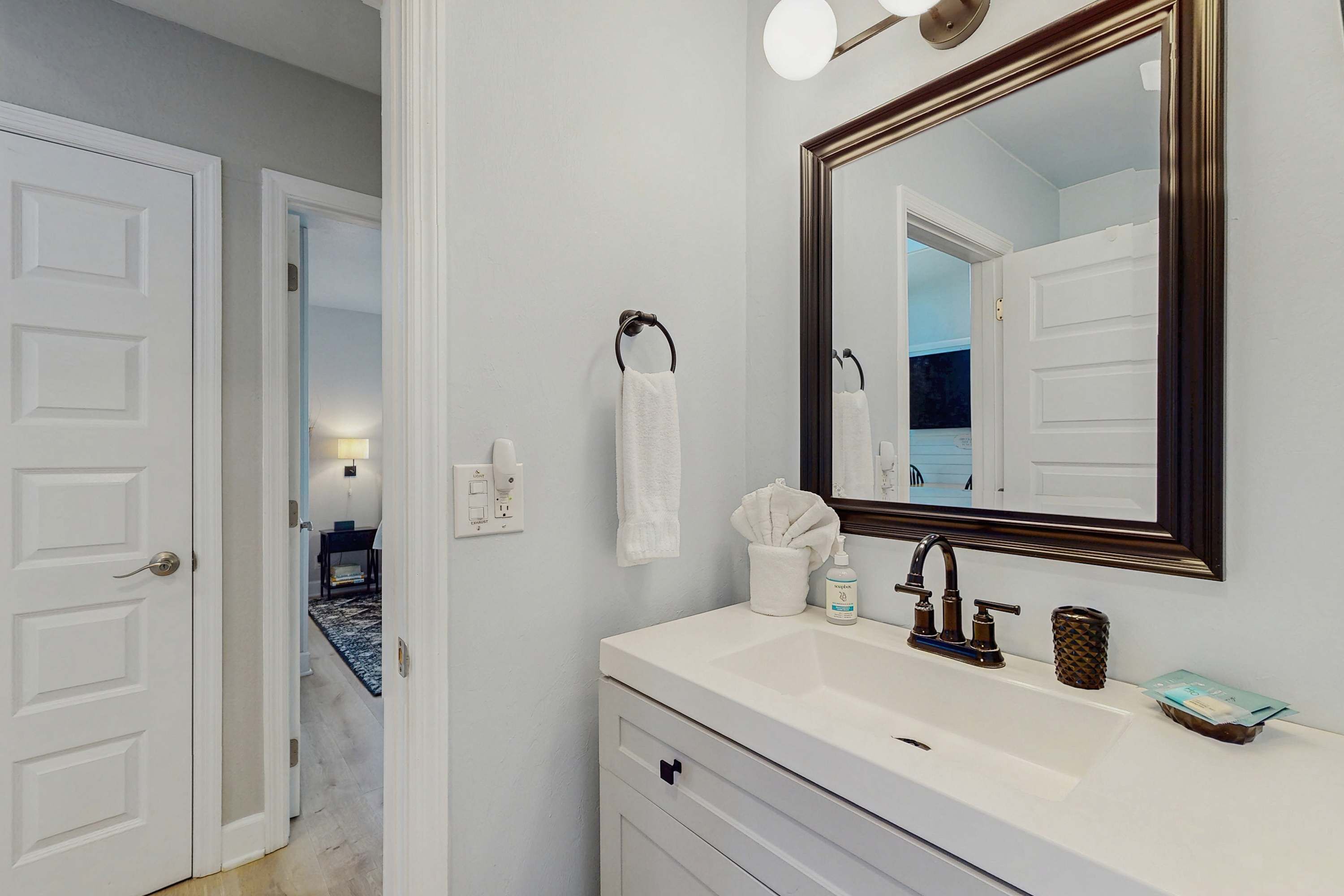 Une salle de bain avec un meuble-lavabo blanc, un grand miroir, un porte-serviettes et un lavabo.