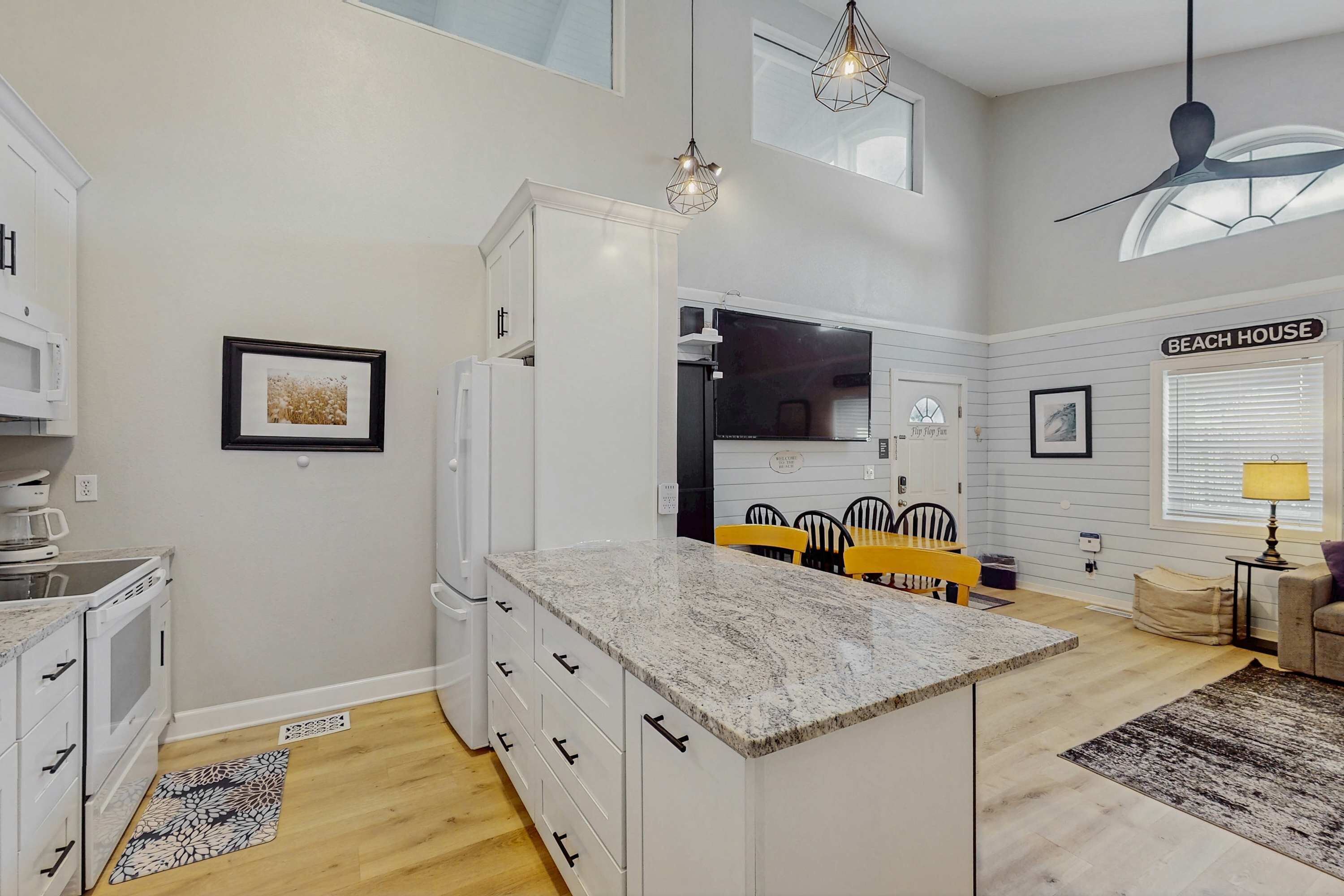 A modern kitchen with white cabinetry, a granite countertop, and a dining area with yellow chairs.