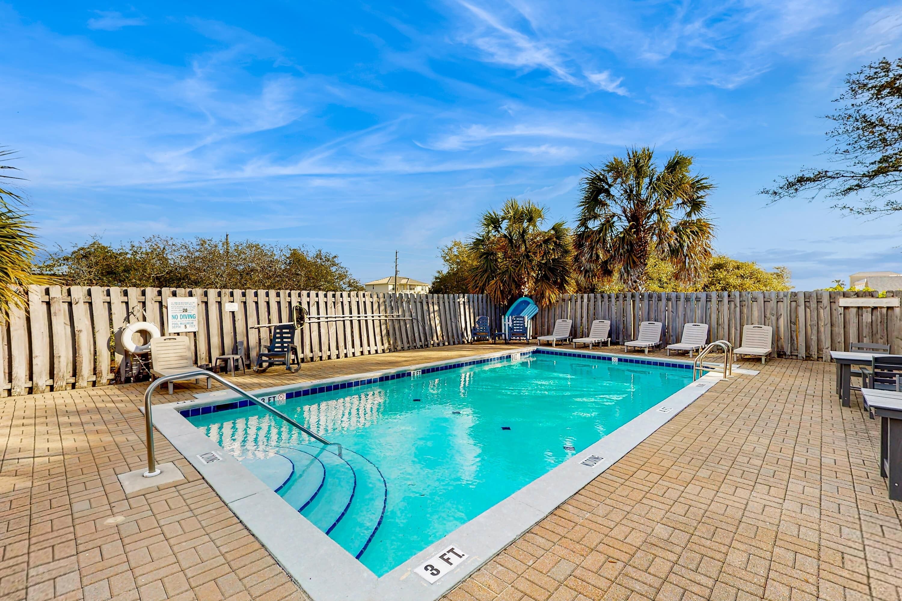 A rectangular outdoor swimming pool with a wooden deck and lounge chairs.
