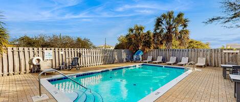 A rectangular outdoor swimming pool with a wooden deck and lounge chairs.