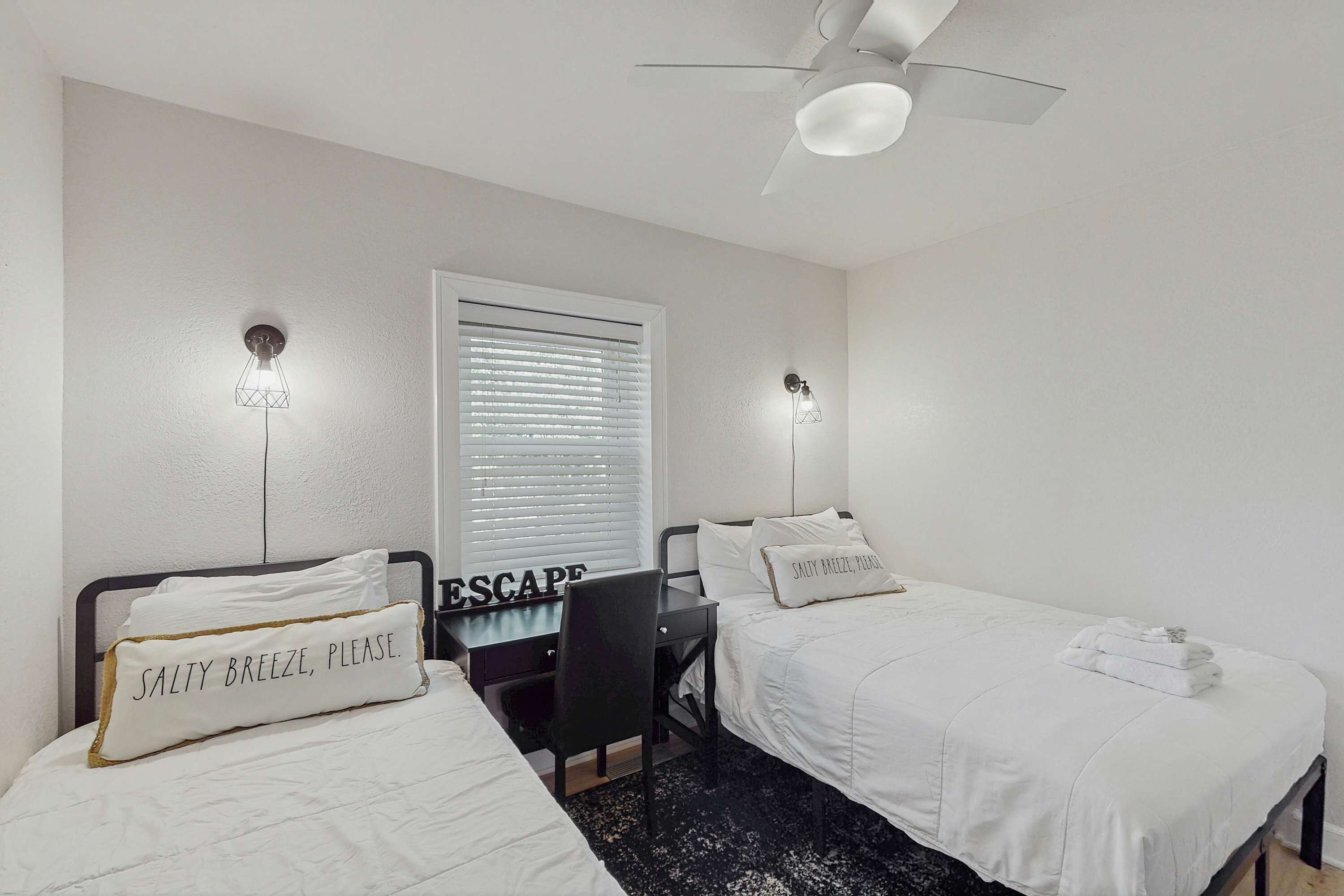 A hotel room with two beds, a desk, and a ceiling fan.