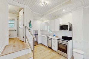 A modern kitchen with white cabinetry, stainless steel appliances, and a wooden floor.