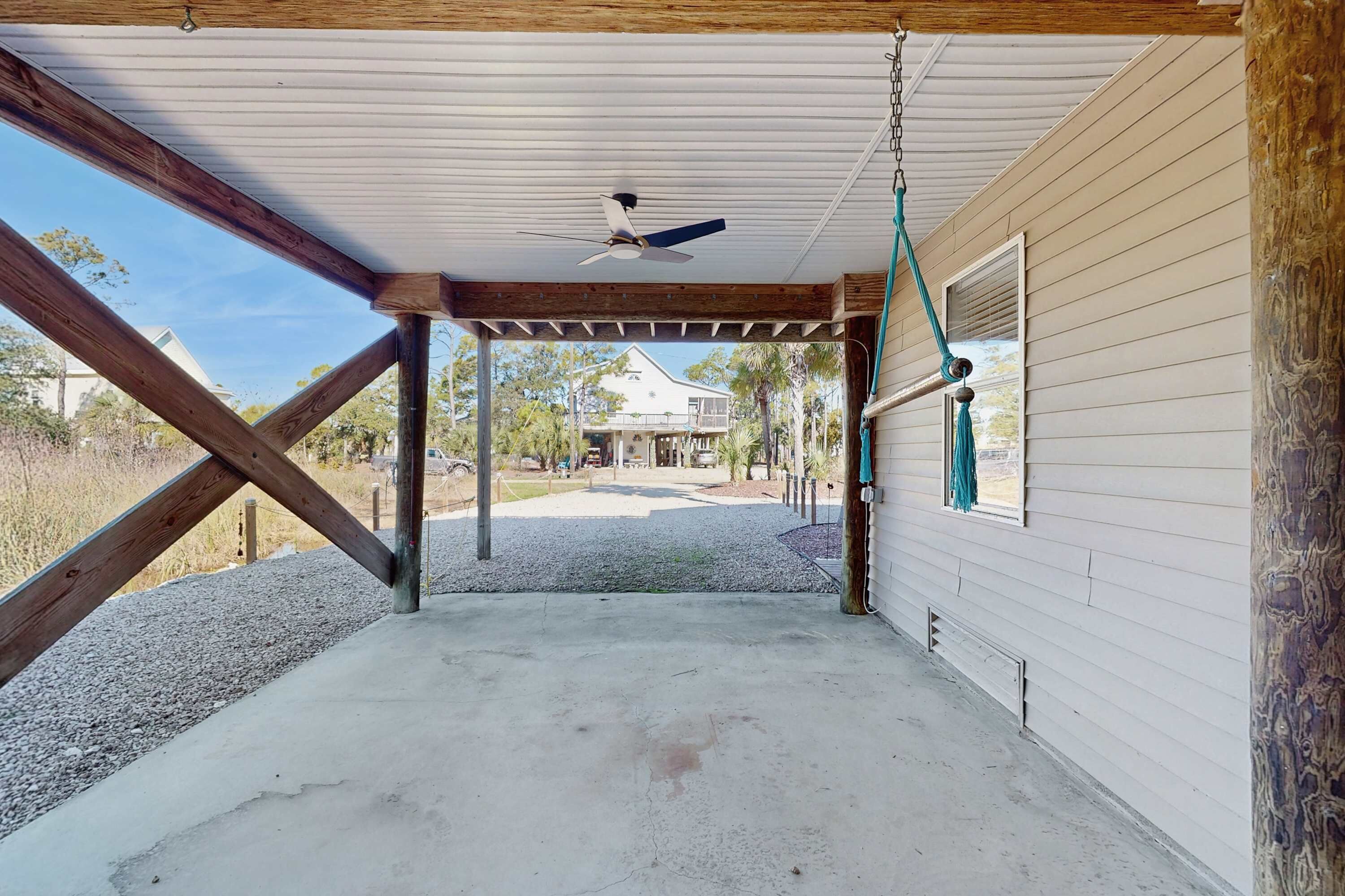 Eine überdachte Veranda mit Deckenventilator, Holzbalken und Betonboden.