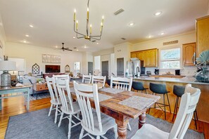 A spacious dining area with a wooden table and white chairs, a kitchen with wooden cabinets, and a ceiling fan. - Beautiful home near the beach with community pool, gym, tennis (St. George Island)