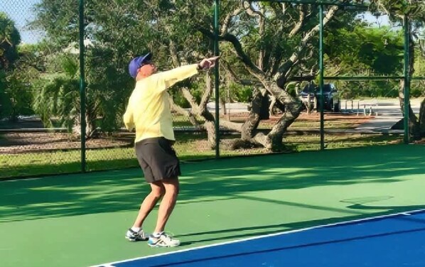 A tennis court with a net, surrounded by a chain-link fence and trees. - Beautiful home near the beach with community pool, gym, tennis (St. George Island)