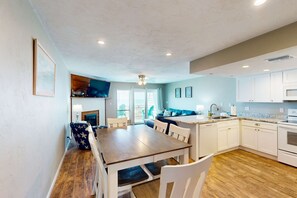 A modern kitchen with white cabinets, a wooden dining table, and a blue sofa. - Beachfront East End townhouse with beach views, deck, on-site pool & grills (St. George Island)