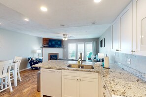 A modern kitchen with a central island, white cabinetry, and a granite countertop. - Beachfront East End townhouse with beach views, deck, on-site pool & grills (St. George Island)