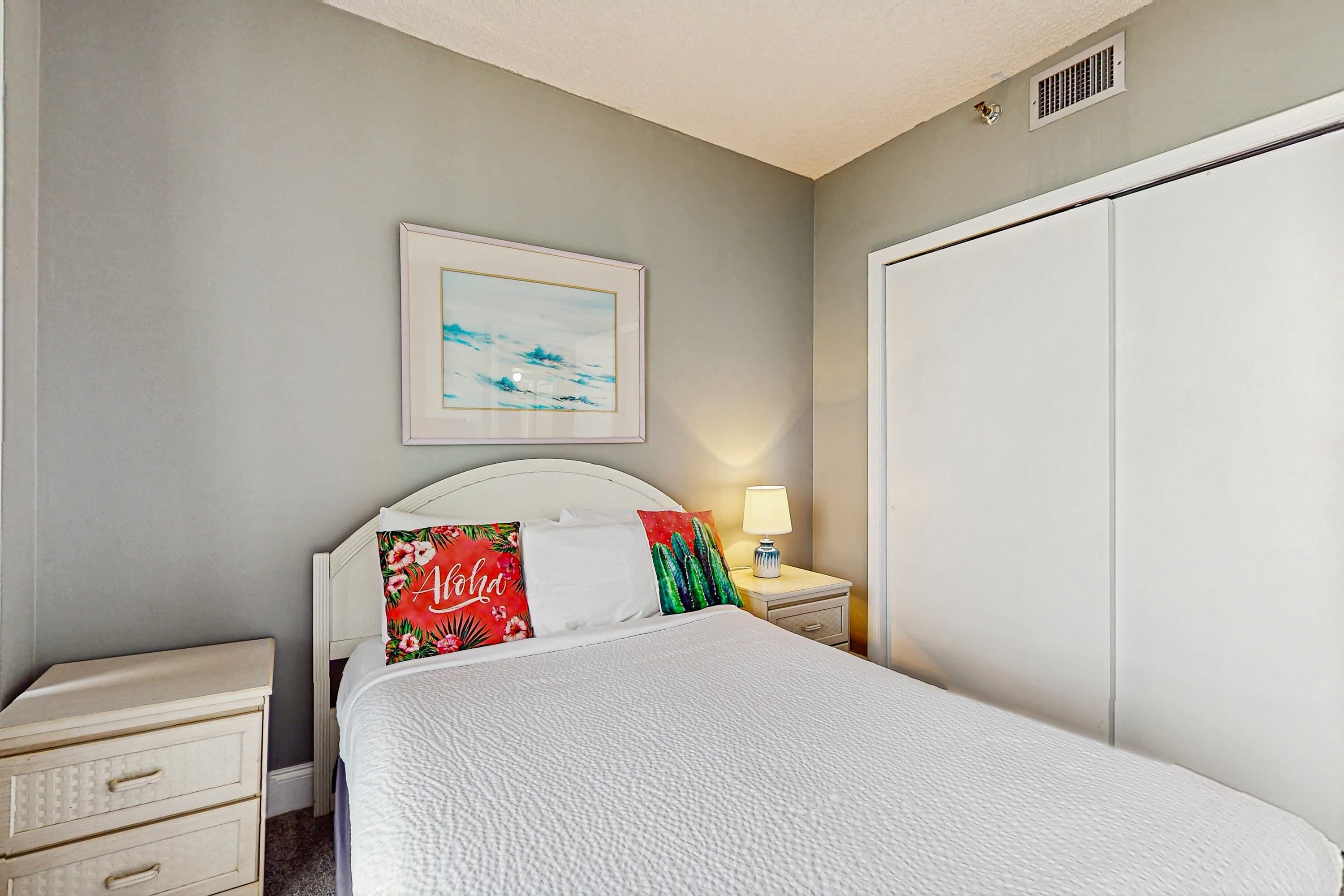 Une chambre à coucher avec un lit, une table de chevet, une lampe, une armoire et un tableau encadré accroché au mur.