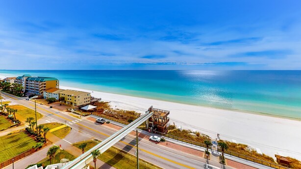 A coastal road with a pedestrian bridge, beach, and buildings. - Second Floor Condo with Shared Pool, Partial Ocean View, Washer/Dryer, and WiFi (Miramar Beach)