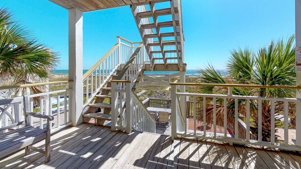 Une terrasse en bois avec un escalier en colimaçon menant à un niveau supérieur, entourée de rampes blanches et de palmiers.