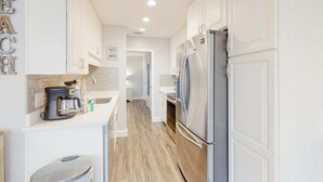 A modern kitchen with white cabinetry, a stainless steel refrigerator, and a coffee maker on the counter. - Ground-floor condo near beach with WiFi, central ac, patio, & onsite pool,tennis (Miramar Beach)