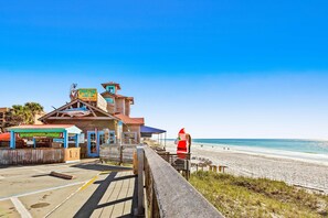 A beachside building with a wooden deck, a lifeguard tower, and a beach view. - Ground-floor condo near beach with WiFi, central ac, patio, & onsite pool,tennis (Miramar Beach)