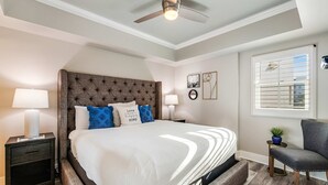 Un dormitorio con una cama grande, dos mesitas de noche, un ventilador de techo y una ventana con persianas.