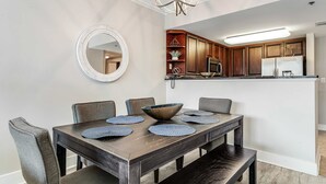Un comedor con una mesa de madera oscura, seis sillas tapizadas grises y un espejo redondo grande en la pared.
