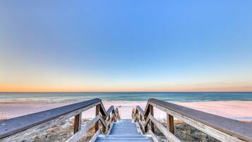 A wooden boardwalk leading to a beach with a clear sky.