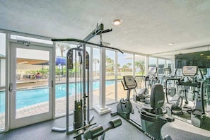 Ein Fitnessraum mit Trainingsgeräten, einem Schwimmbad und großen Fenstern.