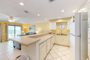 A kitchen with a central island, white cabinets, a clock, and a refrigerator. - 2nd Floor Condo Many Amenities, Beach Access, Beach Equipment Included (Destin)