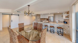Uma cozinha moderna com ilha central, eletrodomésticos embutidos e uma mesa de jantar de vidro com cadeiras de vime.