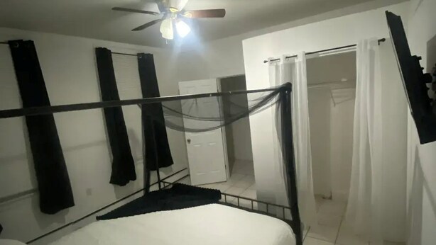 Ein Schlafzimmer mit einem Bett, einem Deckenventilator und einer Tür zu einem Badezimmer.