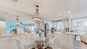 A spacious kitchen with white cabinets, a glass dining table, and a chandelier. - 2nd-floor condo with beach access, pool, tennis courts, & on-site laundry (Destin)