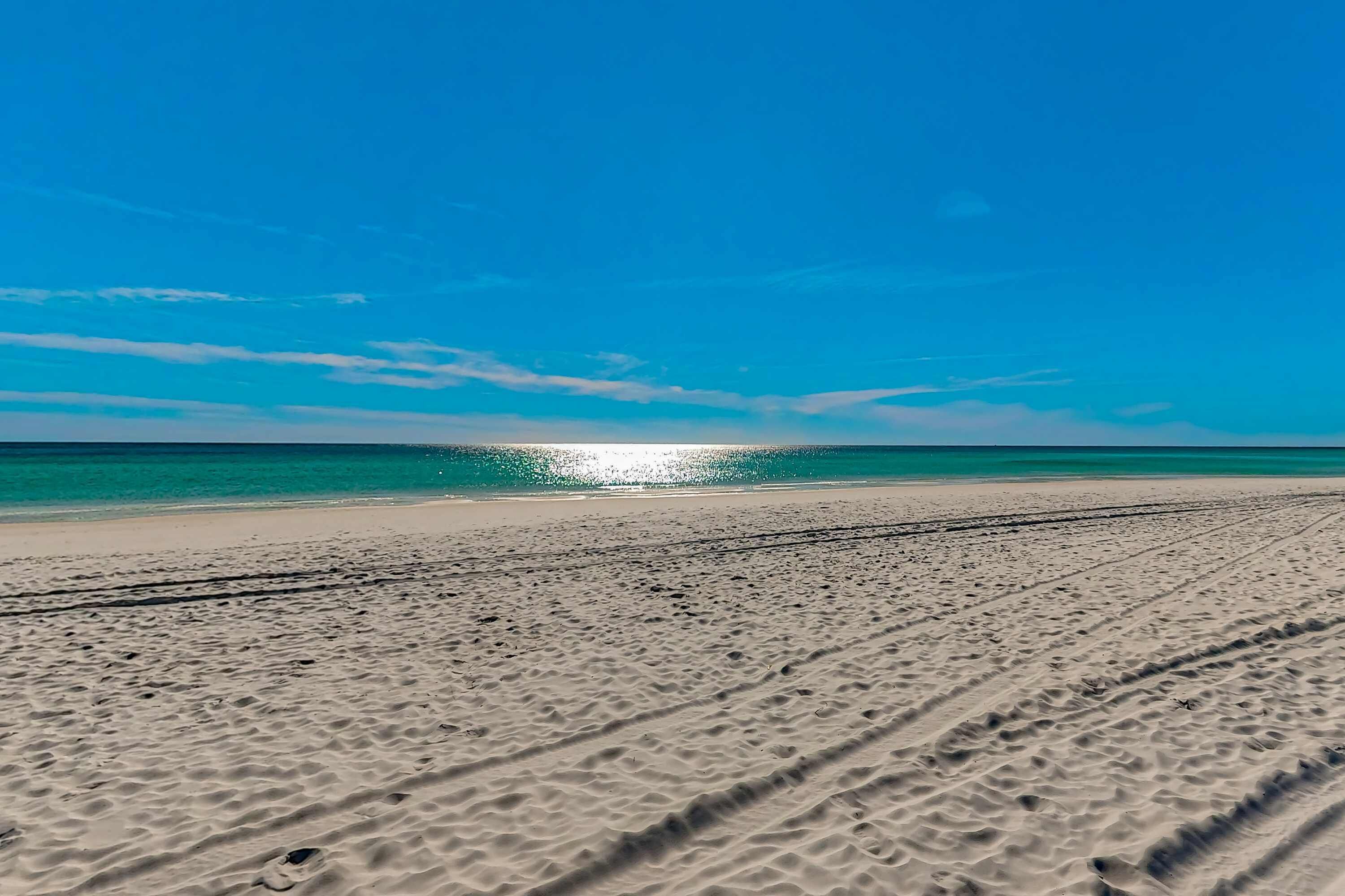 A beach with visible tire tracks and a clear view of the ocean.